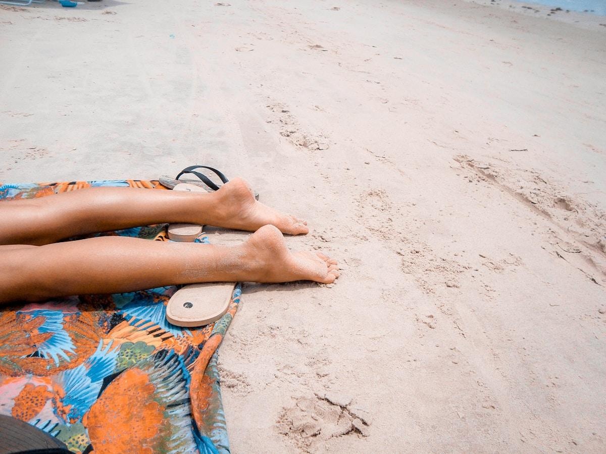 Piernas suaves y depiladas en la playa de verano con sandalias